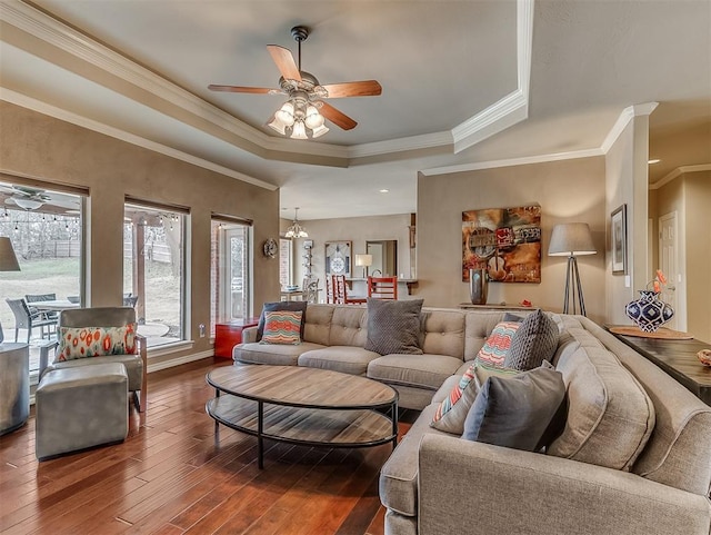 living area with dark wood-style flooring, crown molding, a raised ceiling, baseboards, and ceiling fan with notable chandelier