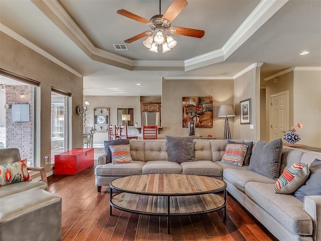 living area with visible vents, a raised ceiling, hardwood / wood-style flooring, ceiling fan, and crown molding