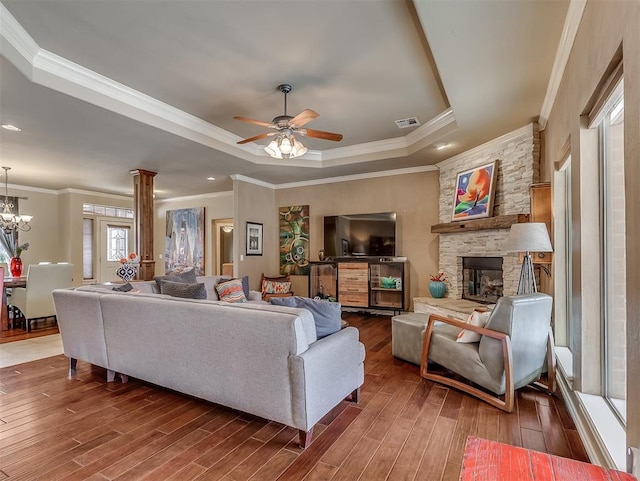 living room with a fireplace, wood finished floors, visible vents, a tray ceiling, and ornate columns