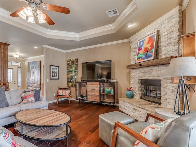 living room featuring a raised ceiling, visible vents, ornamental molding, a stone fireplace, and wood finished floors