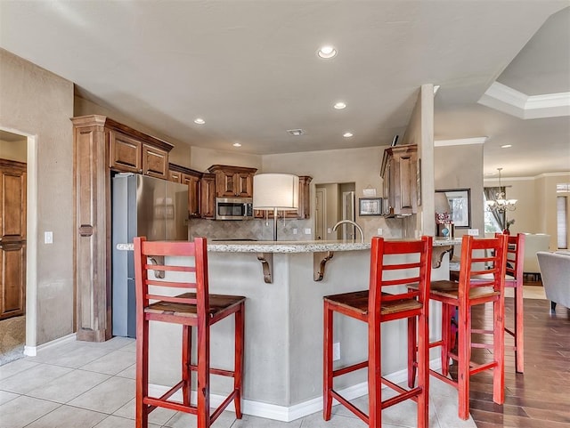 kitchen with backsplash, appliances with stainless steel finishes, light stone countertops, a peninsula, and a kitchen breakfast bar