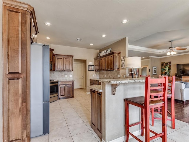 kitchen featuring a kitchen breakfast bar, a peninsula, light stone countertops, stainless steel appliances, and light tile patterned flooring