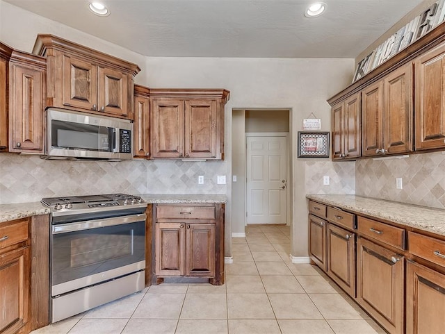 kitchen with light tile patterned floors, appliances with stainless steel finishes, brown cabinets, and light stone counters