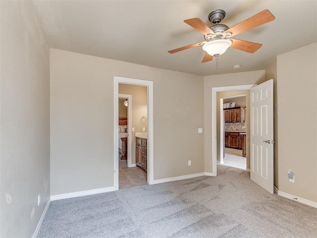 unfurnished bedroom with baseboards, ensuite bath, a ceiling fan, and light colored carpet