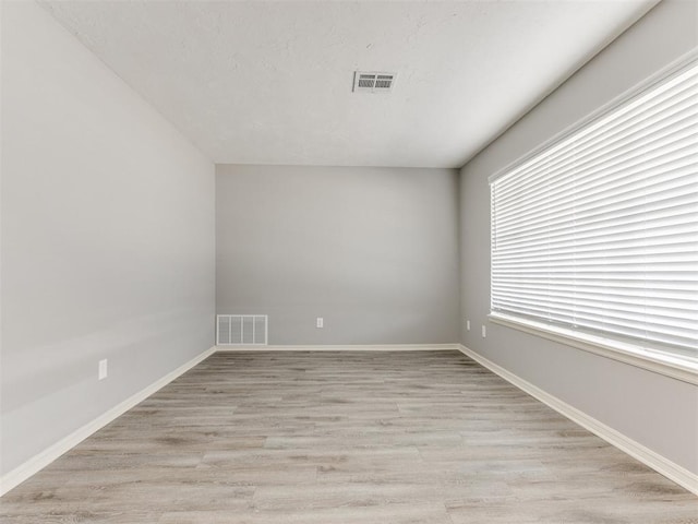 empty room featuring baseboards, visible vents, and light wood finished floors