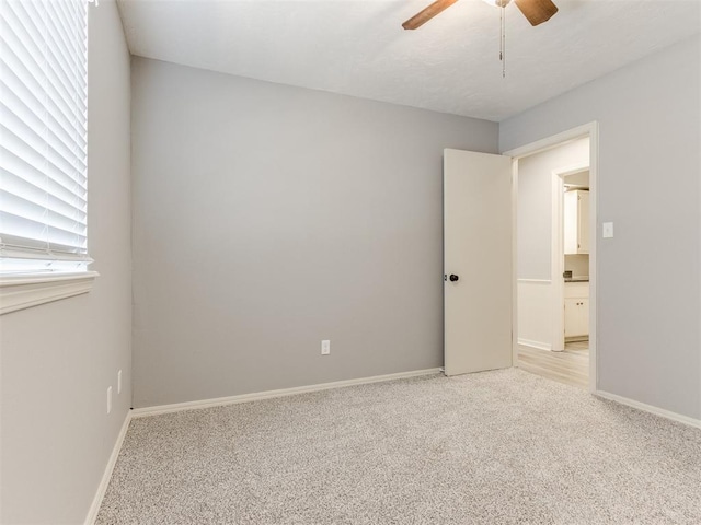 empty room with baseboards, a ceiling fan, and light colored carpet