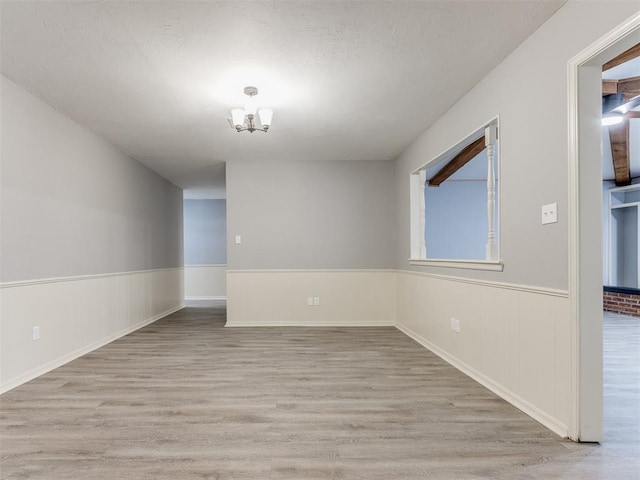 spare room featuring a chandelier, a wainscoted wall, and light wood-style flooring