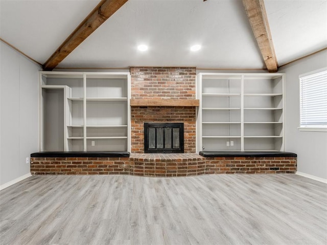 unfurnished living room featuring baseboards, wood finished floors, beamed ceiling, a brick fireplace, and built in shelves