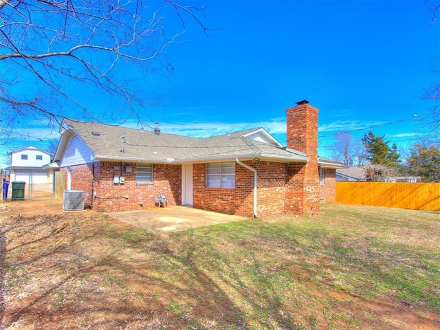 rear view of house featuring brick siding, a yard, a chimney, a patio area, and fence