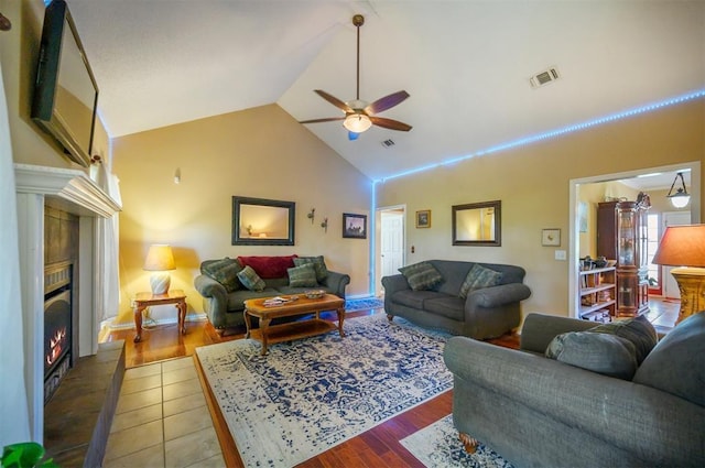 living room with ceiling fan, high vaulted ceiling, tile patterned flooring, a tile fireplace, and visible vents