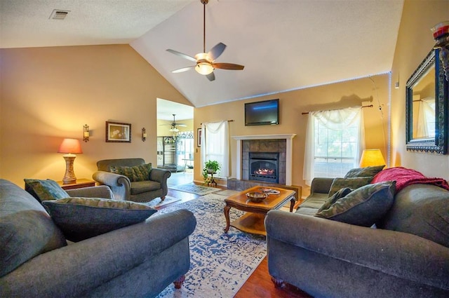 living area with high vaulted ceiling, a tile fireplace, plenty of natural light, and wood finished floors