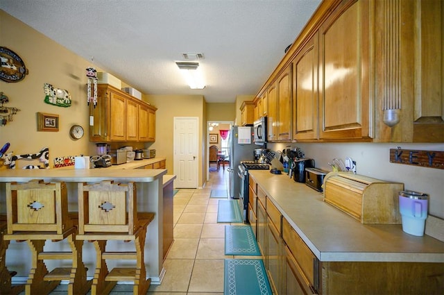 kitchen with stainless steel appliances, brown cabinetry, light countertops, and light tile patterned floors