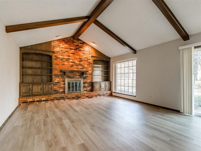 unfurnished living room featuring lofted ceiling with beams, a brick fireplace, plenty of natural light, and built in shelves