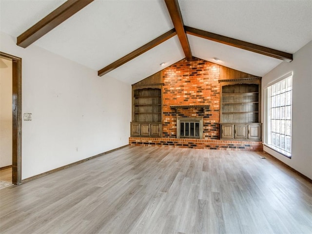 unfurnished living room with built in shelves, a brick fireplace, light wood-style flooring, and lofted ceiling with beams