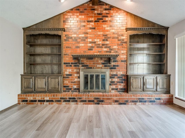 unfurnished living room with vaulted ceiling, built in shelves, a brick fireplace, and wood finished floors