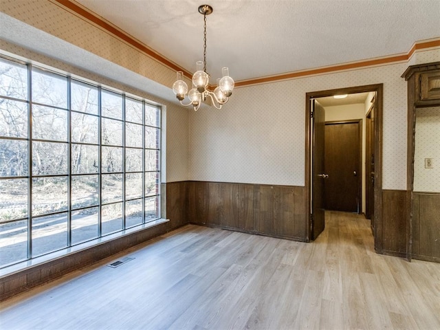 spare room featuring light wood-style flooring, visible vents, ornamental molding, wainscoting, and wallpapered walls