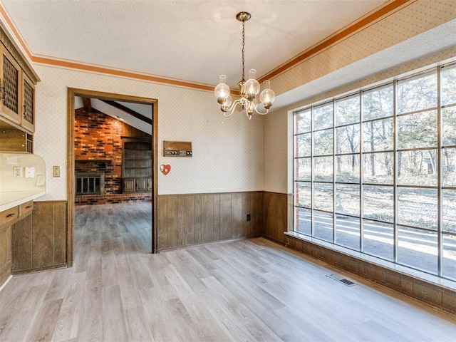 unfurnished dining area featuring ornamental molding, light wood-type flooring, wainscoting, and wallpapered walls