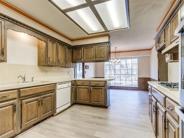 kitchen featuring white dishwasher, a peninsula, ornamental molding, light wood finished floors, and stainless steel gas stovetop