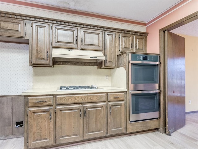 kitchen featuring ornamental molding, light countertops, under cabinet range hood, double oven, and white gas cooktop