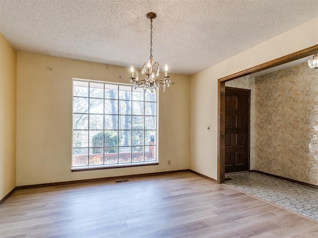 empty room with baseboards, visible vents, wood finished floors, a textured ceiling, and a notable chandelier