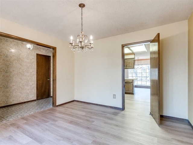 empty room featuring baseboards, a textured ceiling, light wood finished floors, and an inviting chandelier