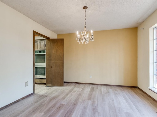 unfurnished room featuring light wood-type flooring, an inviting chandelier, baseboards, and a textured ceiling