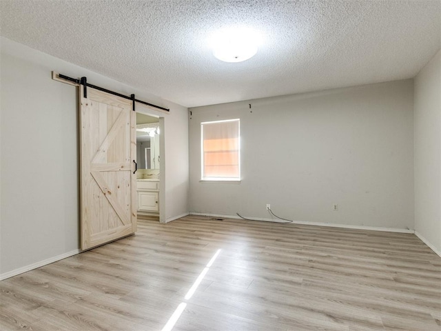 unfurnished bedroom with a textured ceiling, a barn door, light wood-style flooring, and baseboards