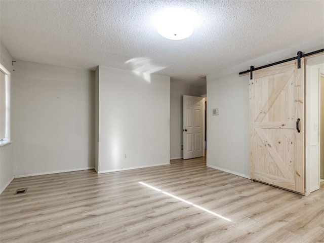 spare room featuring a textured ceiling, a barn door, light wood-type flooring, and visible vents