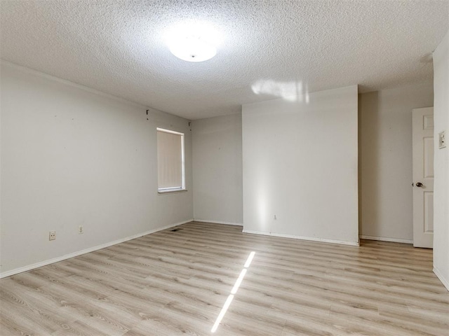 spare room featuring light wood-style flooring, baseboards, and a textured ceiling