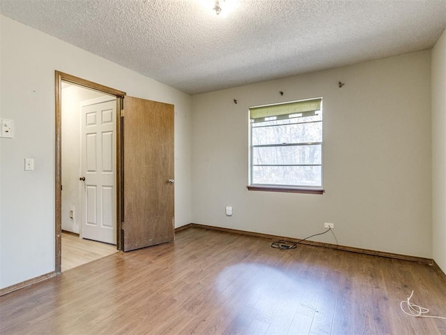 unfurnished room featuring light wood finished floors, baseboards, and a textured ceiling