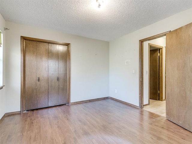 unfurnished bedroom featuring a textured ceiling, a closet, baseboards, and light wood-style floors