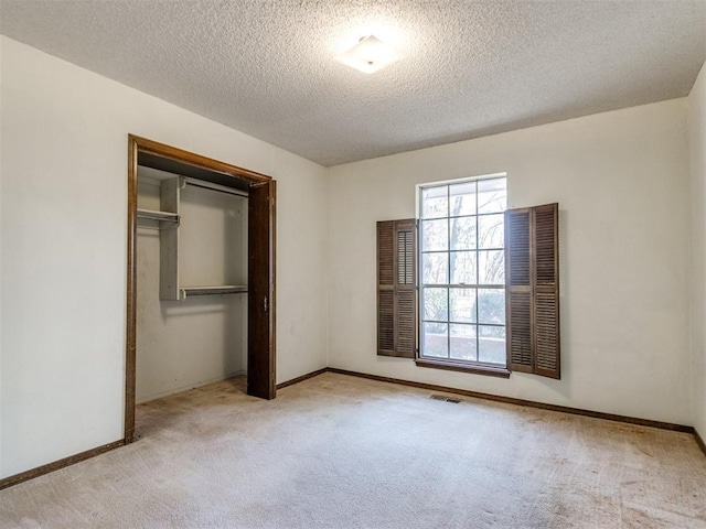 unfurnished bedroom featuring a textured ceiling, carpet flooring, visible vents, baseboards, and a closet