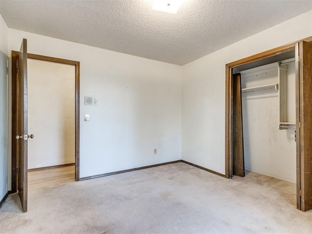 unfurnished bedroom with light carpet, a closet, a textured ceiling, and baseboards