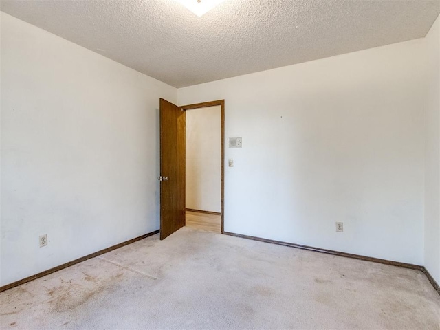 spare room with light carpet, a textured ceiling, and baseboards