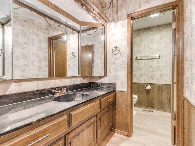 bathroom featuring toilet, a wainscoted wall, visible vents, vanity, and wallpapered walls