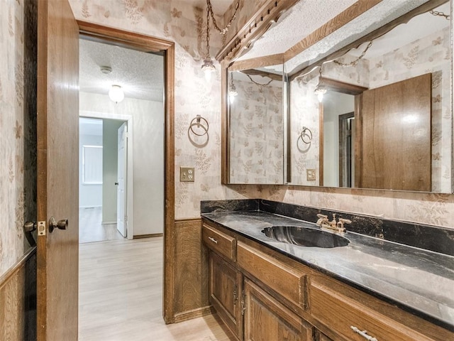 bathroom featuring wallpapered walls, vanity, a textured ceiling, and wood finished floors