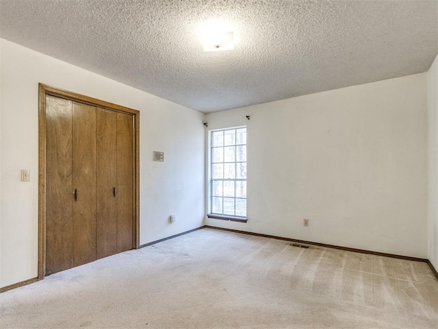 unfurnished bedroom featuring a closet, visible vents, carpet flooring, a textured ceiling, and baseboards