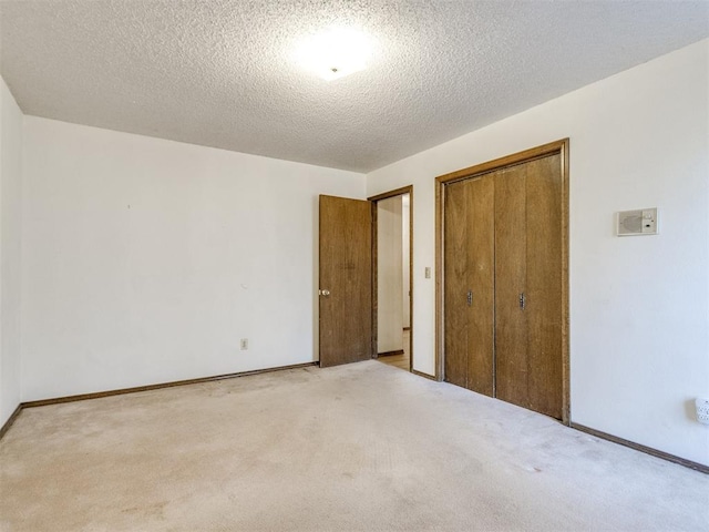 unfurnished bedroom featuring light carpet, a closet, a textured ceiling, and baseboards