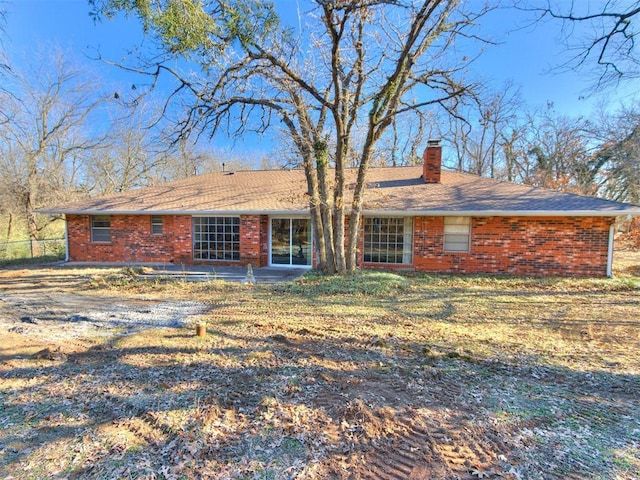 back of property with a chimney, fence, and brick siding