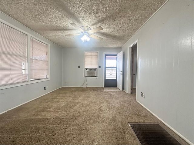 carpeted spare room featuring a textured ceiling, cooling unit, visible vents, baseboards, and a ceiling fan
