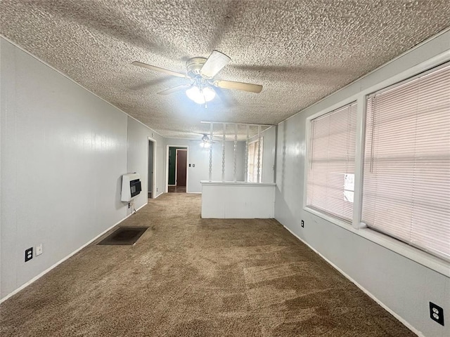 spare room featuring a textured ceiling, ceiling fan, carpet floors, visible vents, and heating unit