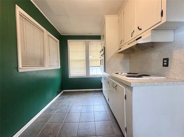 kitchen featuring white cabinets, white electric cooktop, under cabinet range hood, dark tile patterned floors, and stainless steel oven