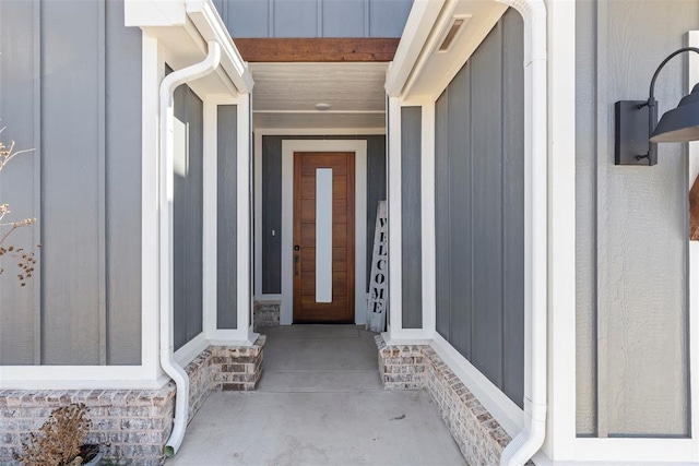 view of exterior entry with board and batten siding and visible vents