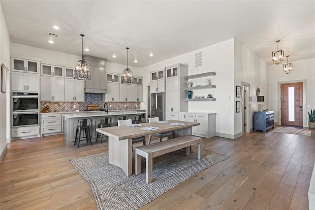 kitchen featuring a center island with sink, a notable chandelier, a breakfast bar area, open shelves, and appliances with stainless steel finishes