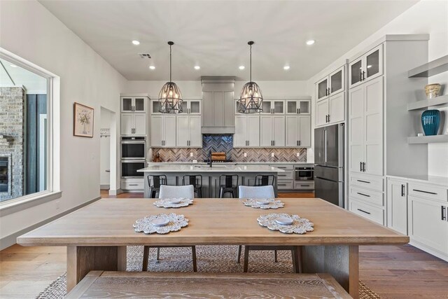 kitchen featuring a center island with sink, wood finished floors, stainless steel appliances, light countertops, and white cabinetry