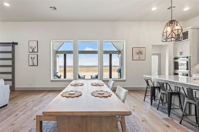 dining area with light wood finished floors, a barn door, visible vents, and a notable chandelier