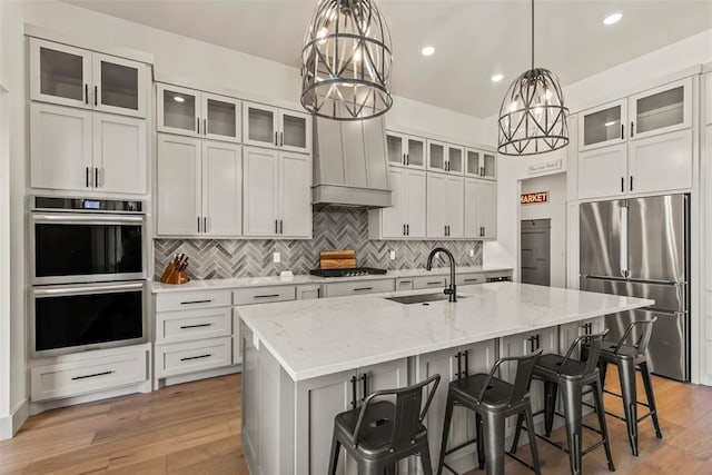 kitchen with a sink, a kitchen breakfast bar, appliances with stainless steel finishes, light wood finished floors, and an island with sink