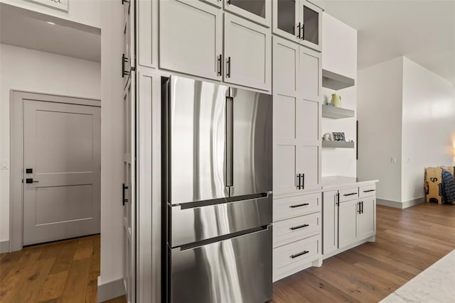 kitchen featuring wood finished floors, light countertops, open shelves, stainless steel fridge, and glass insert cabinets