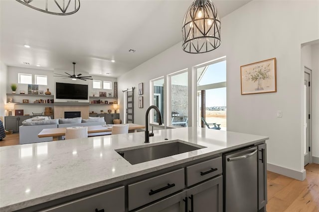 kitchen featuring pendant lighting, a fireplace, stainless steel dishwasher, a sink, and ceiling fan with notable chandelier