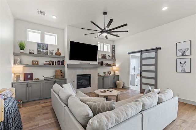 living room with ceiling fan, a barn door, recessed lighting, light wood-style floors, and a glass covered fireplace